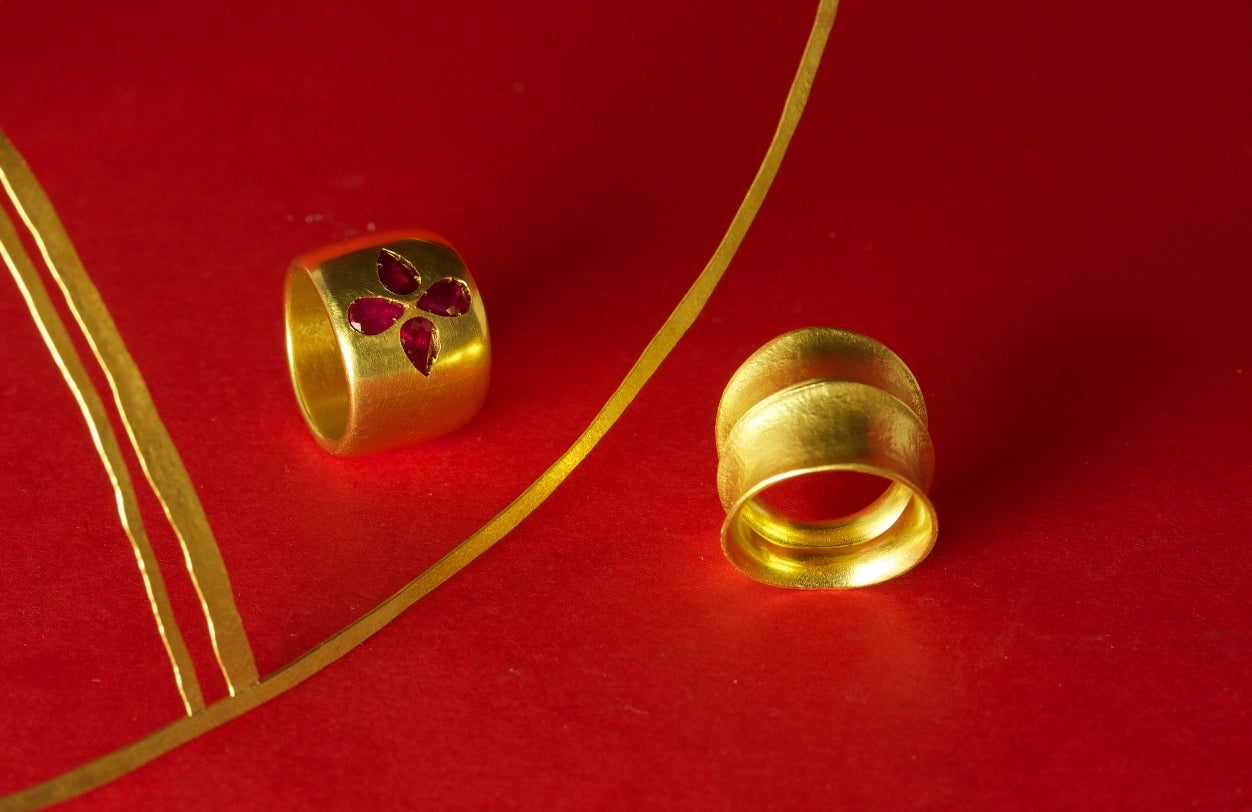 Daedalus ruby ring, Zambesi ring. Khalakahl armbands. 18ct yellow gold. On a red backdrop with soft gentle shadows.