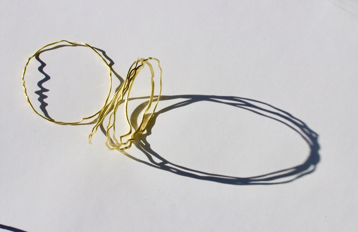 Sirena bangles. 18ct yellow gold. With its shadow dark and intense on the white background.