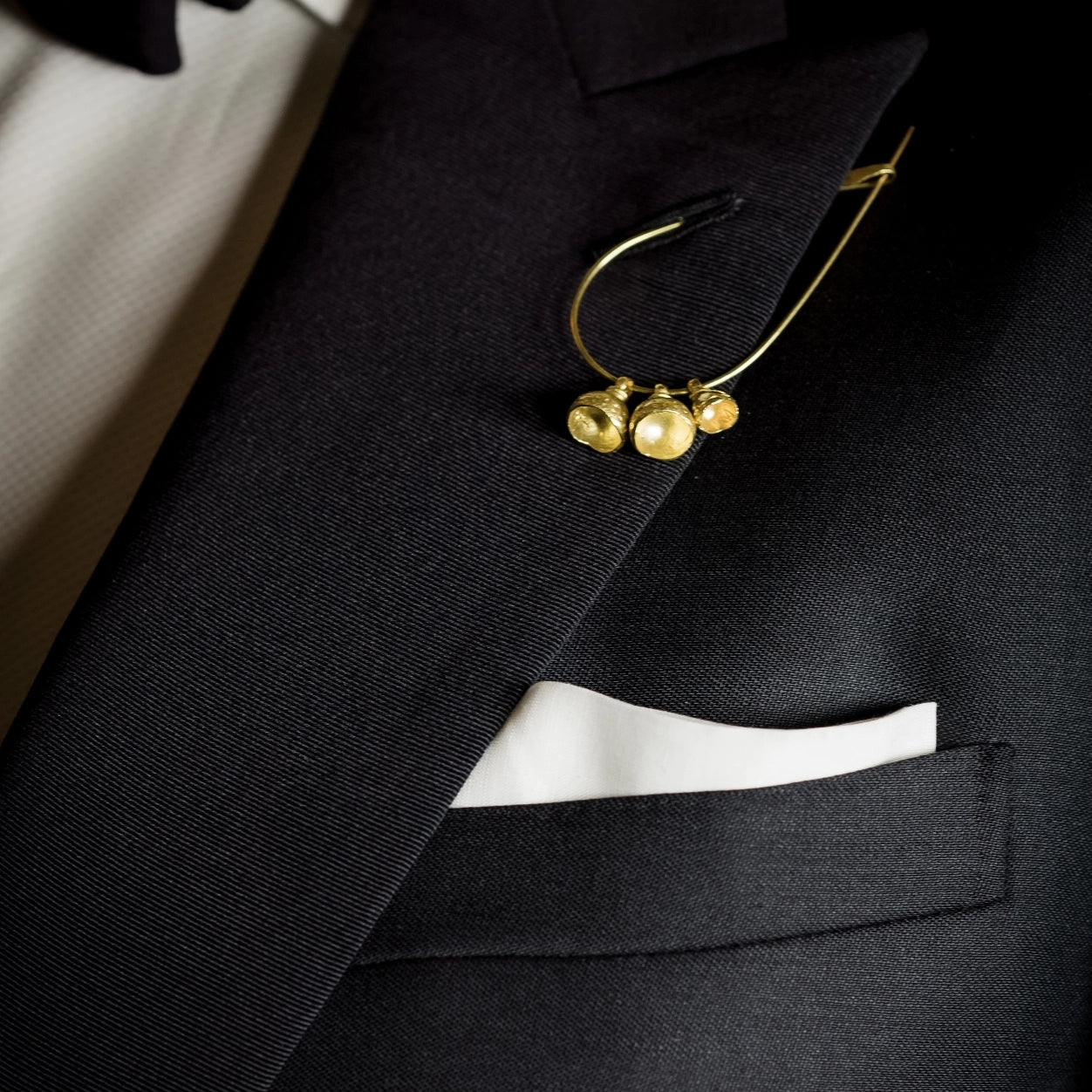 Wright & Teague Tempo bells pin. 18ct Fairtrade gold. Worn through the button hole of a dark grey suit.