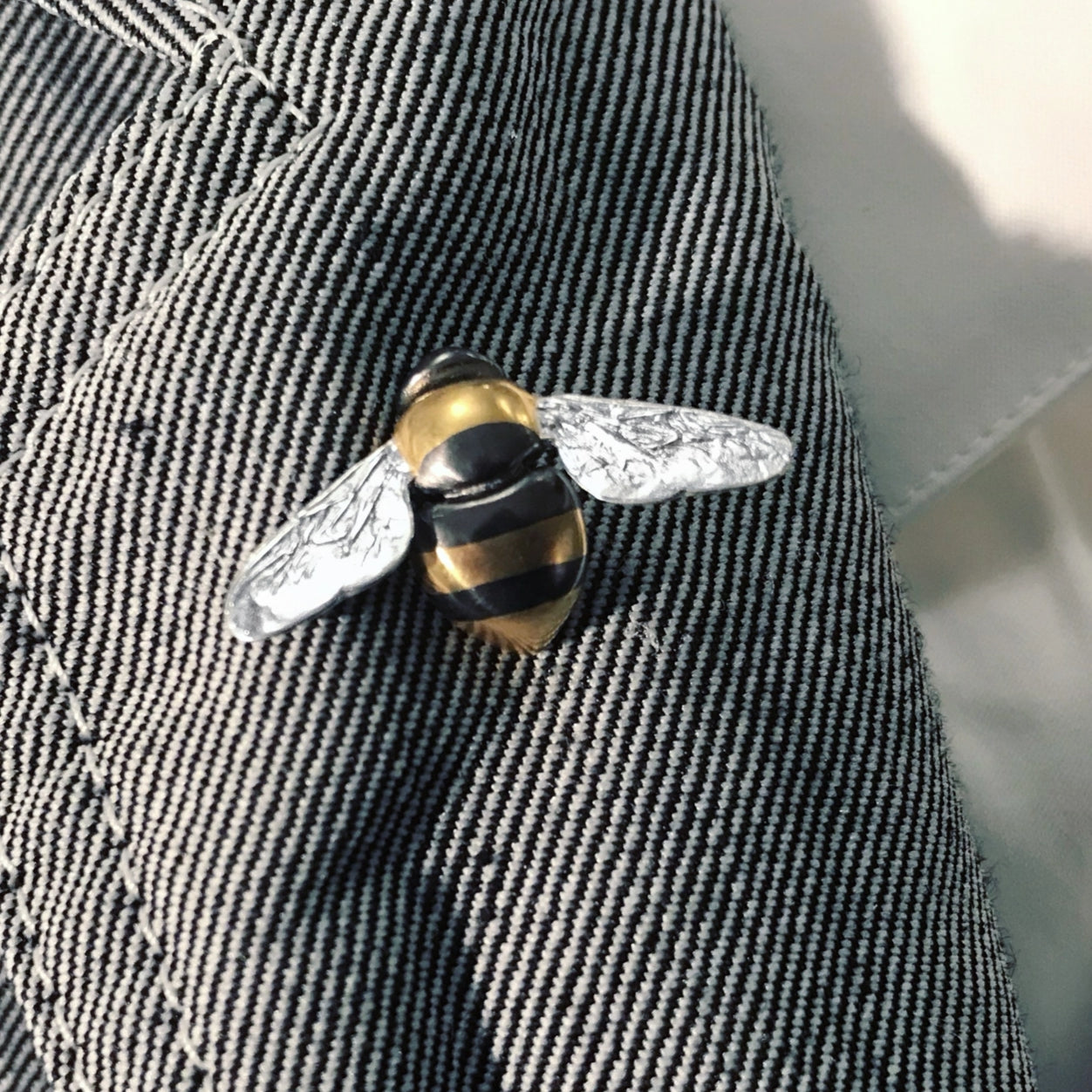 Wright & Teague Bee striped pin. Silver, gold vermeil, black rhodium. Worn on the lapel of a light jacket.