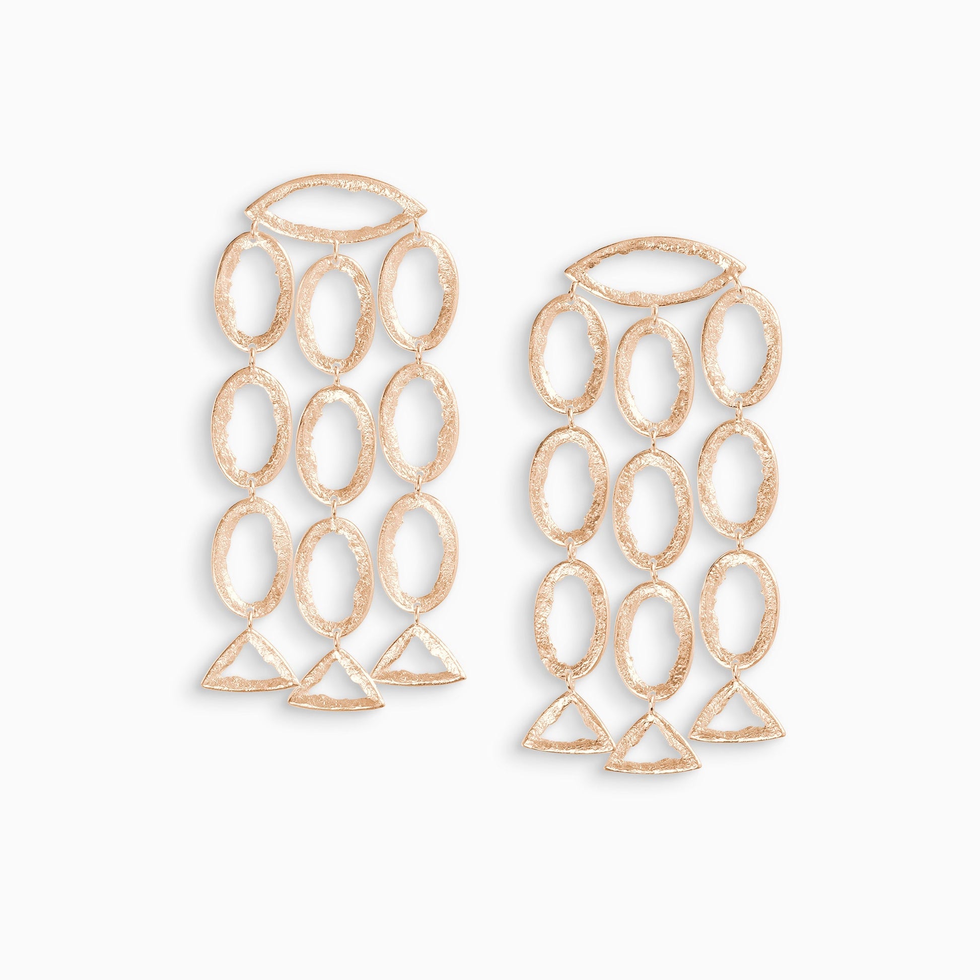 A pair of 18ct Fairtrade rose gold drop earrings. 3 parallel lines of articulating oval shapes hang from a horizontal lozenge shape with a stud ear fastening. These open shapes have a strong organic texture and are smooth on the outside edges with fragmented inside edges. 76mm length. 40mm width.