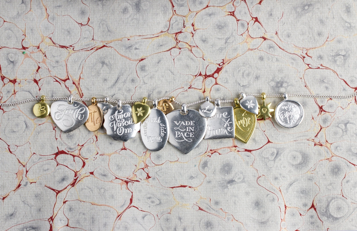 Inscription pendants. Silver and 18ct gold. laying on a ink dyed fabric.