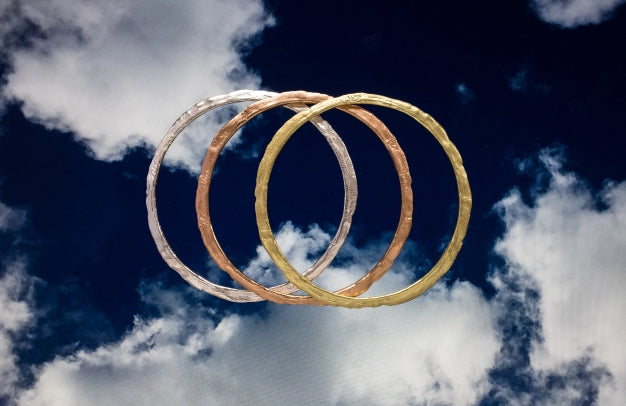 Eclipse bangles.Silver and 18ct rose and yellow gold. Floating in a cloudy blue sky.