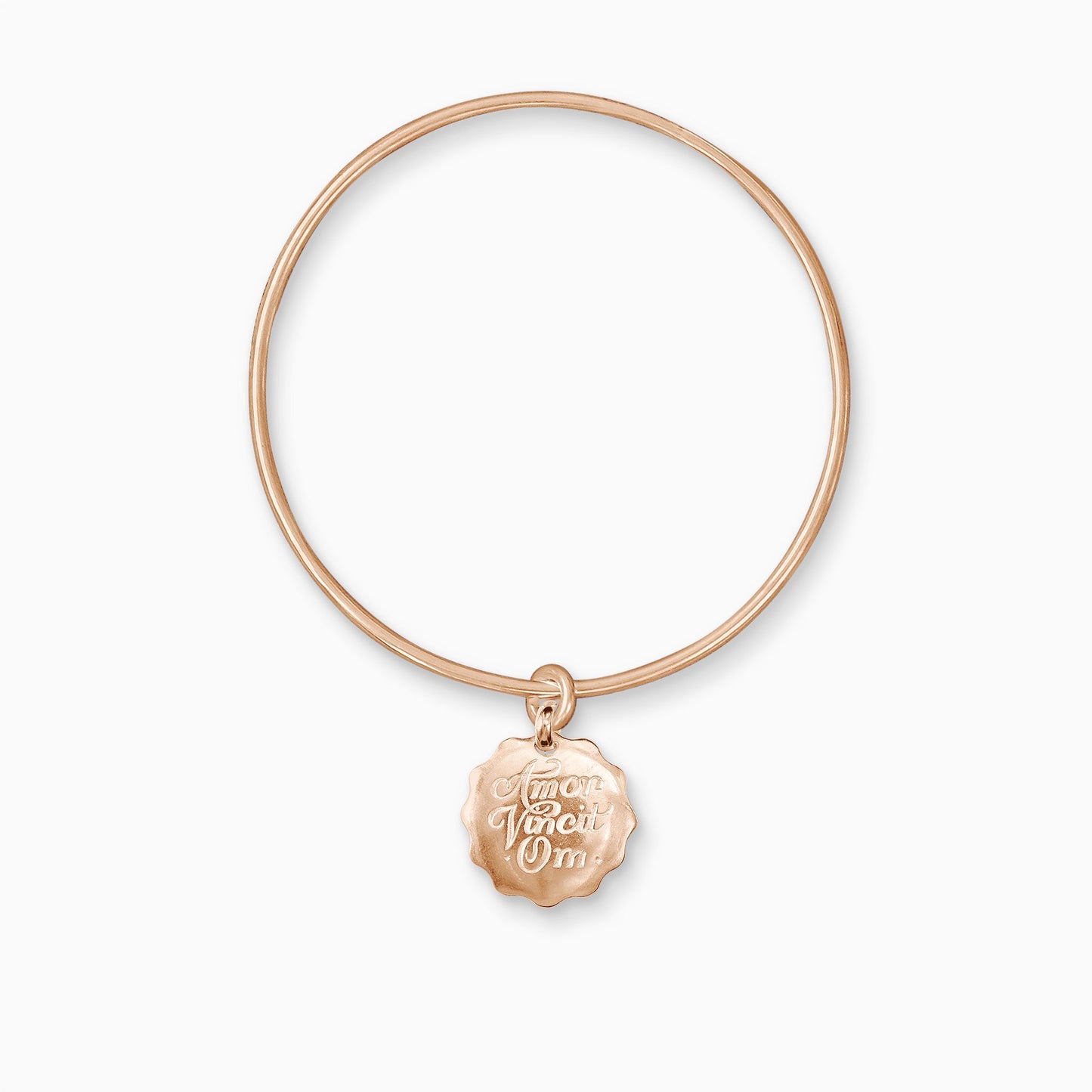 An 18ct Fairtrade rose gold round, smooth charm with a wavy edge engraved with ‘Love Conquers All’ in Latin, freely moving on a round wire bangle.  Charm 22mm. Bangle, 63mm inside diameter x 2mm round wire.