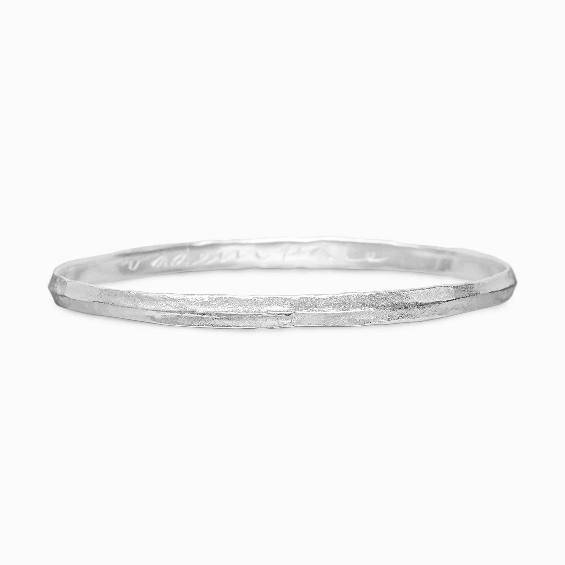 A recycled Silver bangle rising to a central ridge, engraved inside ‘VAde in Pace’ which is ‘Go in Peace’ in Latin. Width 5mm. Inside diameter 63mm.