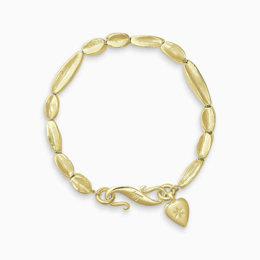 An 18ct Fairtrade yellow gold bracelet of handmade organic, concave, square section textured ‘Baluba’ beads. Finished with a smooth heart shaped charm, engraved with a 6 petal flower and our signature ’S’ clasp.Bracelet length 210mm.. Beads varying lengths from 10mm to 40mm. Cross section of each bead approximately 6mm.