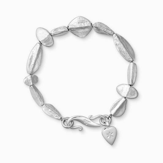 A recycled Silver bracelet of handmade textured beads with a central ridge.  Finished with a smooth heart shaped charm engraved with a 6 petal flower and our signature ’S’ clasp.Bracelet length 210mm. Beads varying sizes from 11mm x 6mm to 35mm x 15mm.