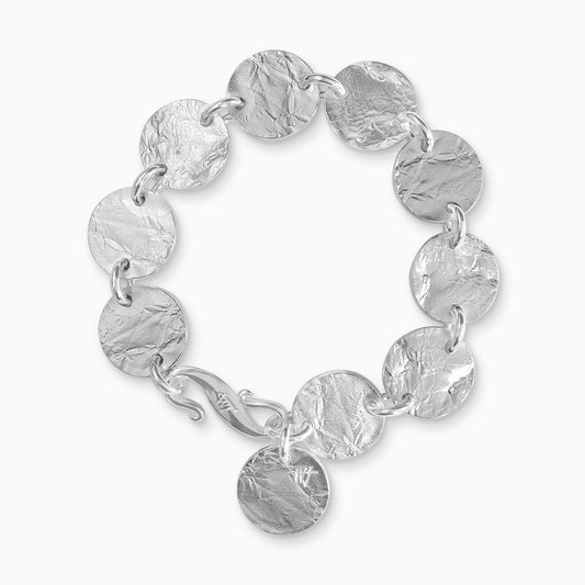 A recycled Silver bracelet of 9 linked textured discs with a 10th suspended near the large ’S’ clasp. Discs 17mm diameter. Bracelet length 190mm.