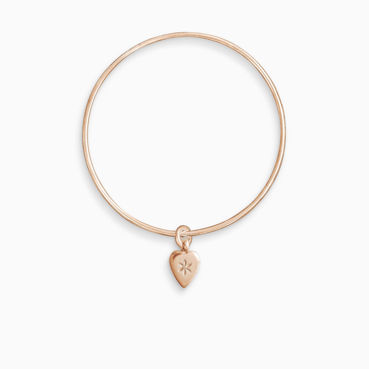 An 18ct Fairtrade rose gold smooth heart shaped charm engraved with a 6 petal flower, freely moving on a round wire bangle. Charm 15mm x 8mm. Bangle 63mm inside diameter x 2mm round wire.