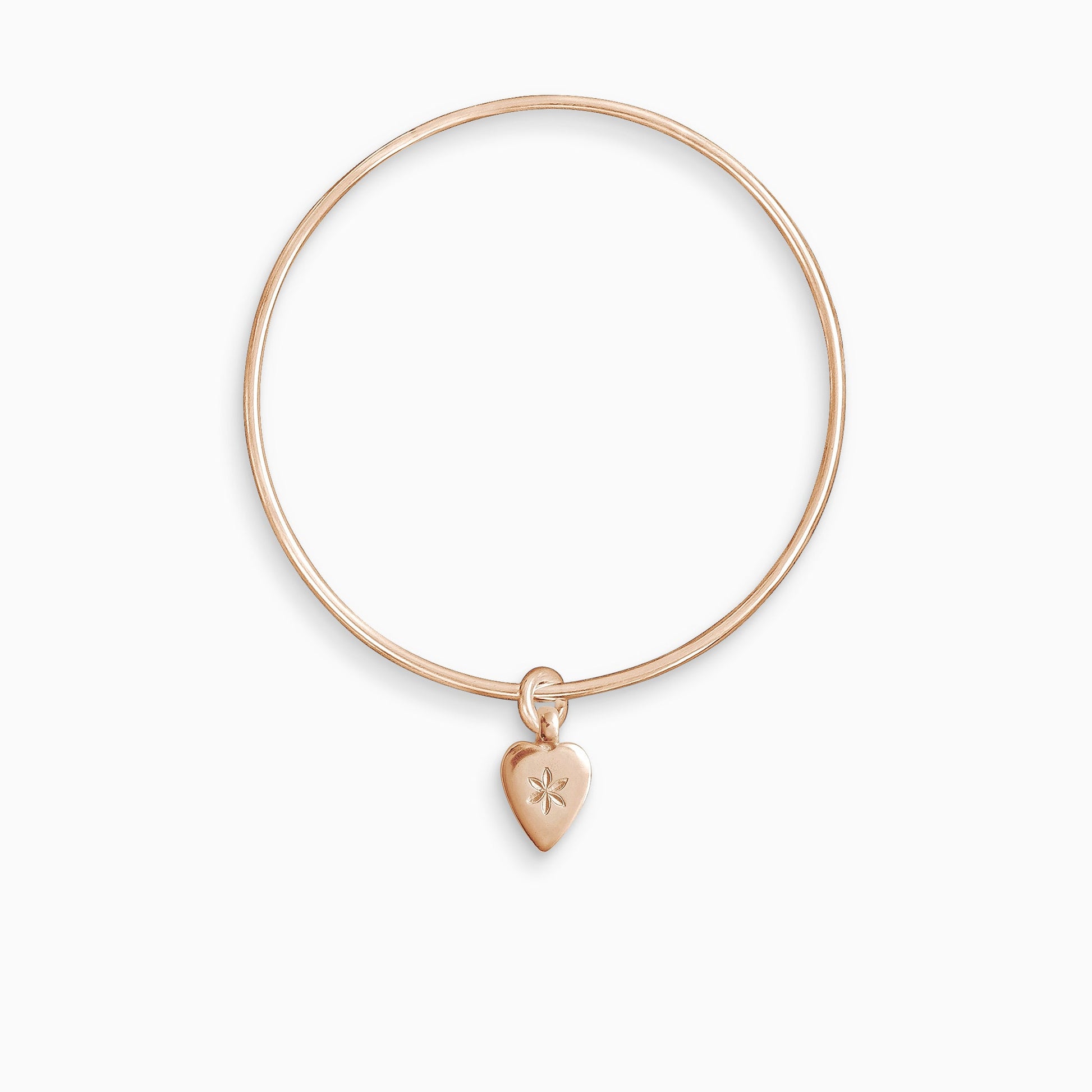 An 18ct Fairtrade rose gold smooth heart shaped charm engraved with a 6 petal flower, freely moving on a round wire bangle. Charm 15mm x 8mm. Bangle 63mm inside diameter x 2mm round wire.